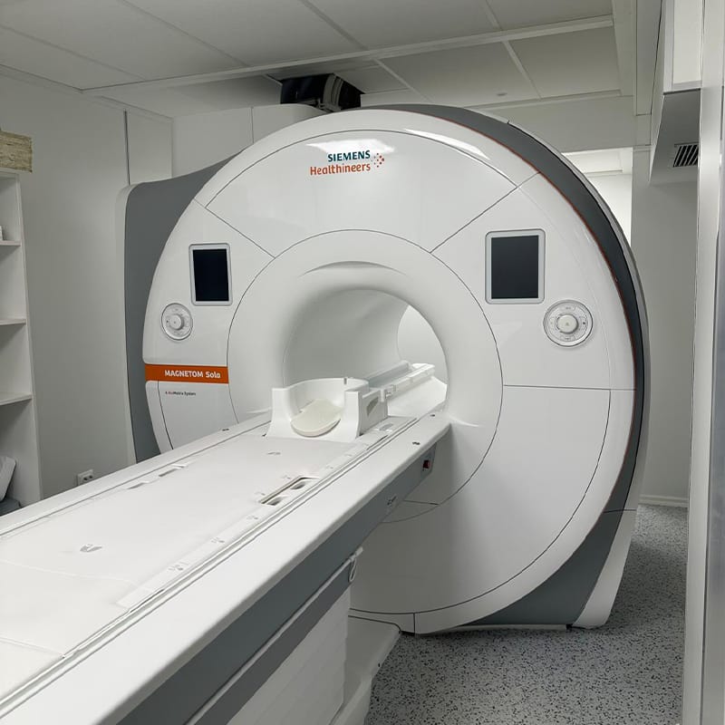 Un aparat RMN Siemens Healthineers mare, alb, cu un pat glisant pentru pacient este poziționat într-o sală medicală curată și modernă la Clinica Medicala Grama.